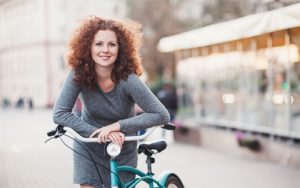 A woman with curly red hair, riding a bike to keep healthy.